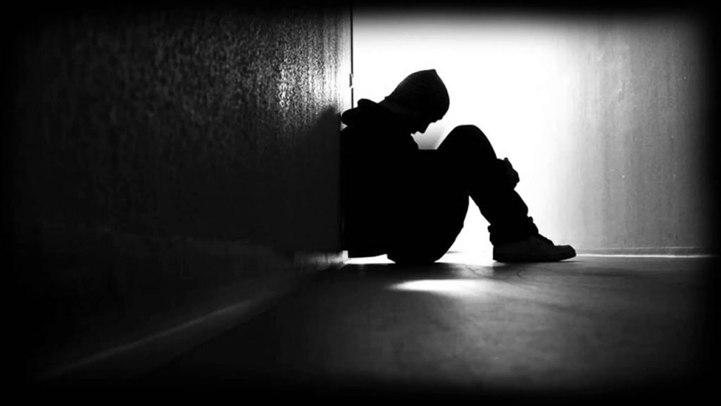 Silhouette of a man huddled in a corner of a hall looking emotional