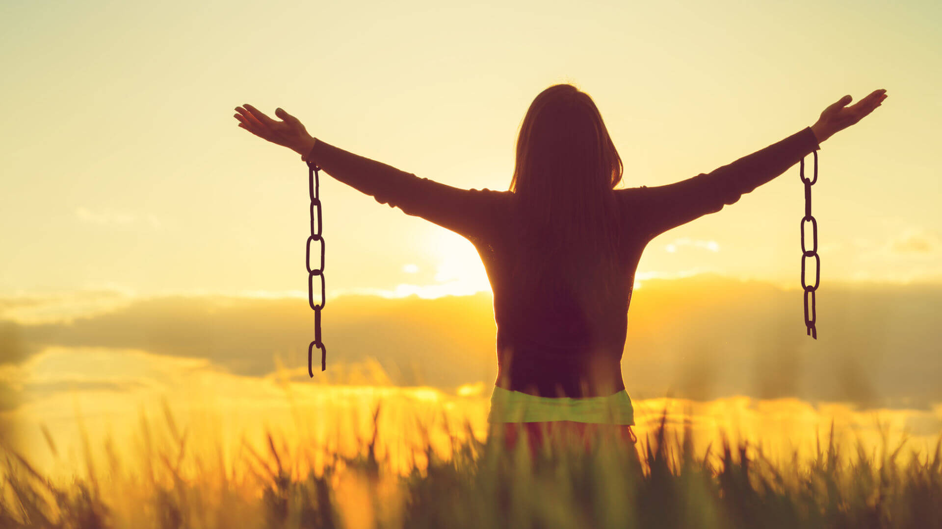 A woman shown from the back with broken chains hanging off her wrists depicting freedom from emotional issues