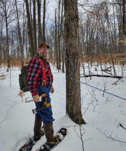 Photo showing Dave with his snow shoes on, working in the woods on his maple business.